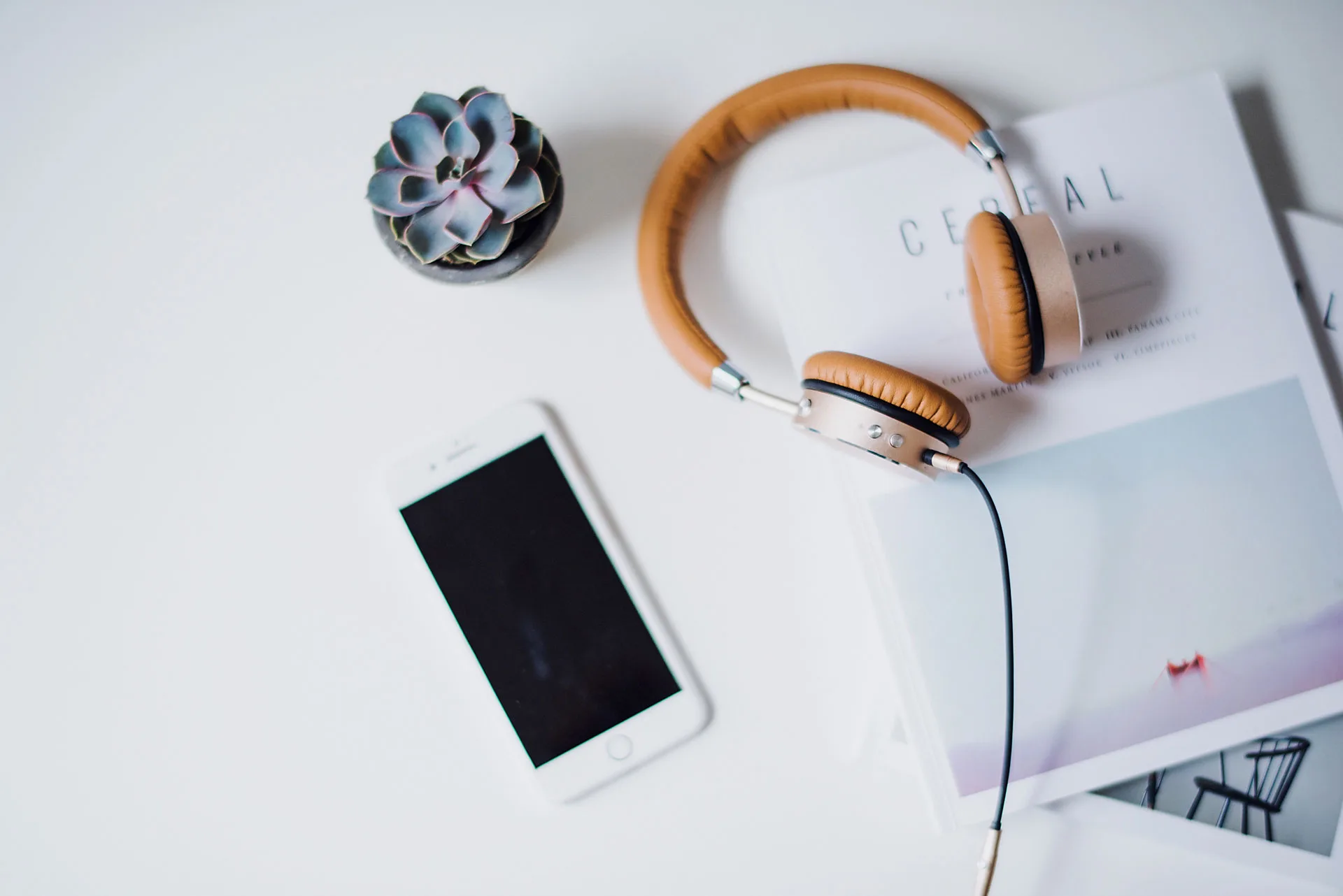 Flatlay of headphones, a phone, and a magazine on a desk