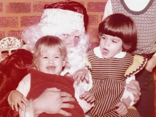 A vintage photo of a crying toddler on Santa's lap, with two other children beside him
